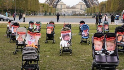 法国巴黎埃菲尔铁塔前的战神广场周四举行示威活动期间，在一堆婴儿车上展示了本月7日在以色列遭巴勒斯坦伊斯兰抵抗运动（哈马斯）掳走的年轻人质照片。（图取自法新社）