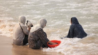 在加沙地带南部代尔巴拉赫的海滩上，由于缺乏淡水和电力，巴勒斯坦妇女在周日用海水洗衣服。（图取自法新社）