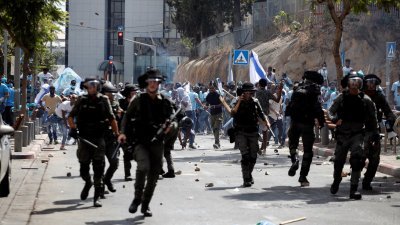 以色列警方被厄立特里亚难民投掷石头，要向后撤退，大批手持铁棍及铁槌的人则从后追赶。（图取自路透社）