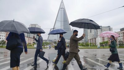 朝鲜民众在雨中撑伞走过平壤街头，远处为平壤的标志性建筑柳京酒店。（图取自共同社/路透社）