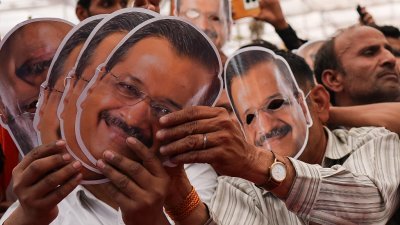 周日在新德里举行的集会，印度反对党联盟的支持者高喊口号，并手持平民党主席、德里首席部长凯杰里瓦尔肖像的面具及展示标语牌。（图取自法新社）