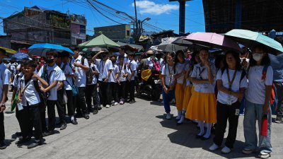 菲律宾首都马尼拉一所学校的学生，周二在学校外手持雨伞排队等待上课。（图取自法新社）