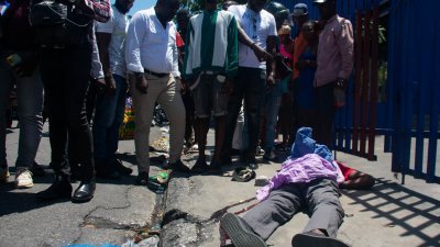 在海地首都太子港，民众周一围观一具躺在地上遭枪杀的尸体。（图取自法新社）