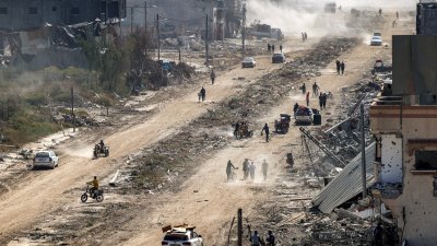 以军当地时间周日宣布从加沙地带南部撤出地面部队，巴勒斯坦人当天走过汗尤尼斯一条道路，两边都是因战争被毁坏的建筑物。（图取自法新社）