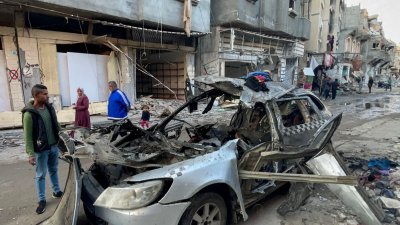 有路人在周三看著一辆遭以军空袭而毁不成形的汽车残骸，据报这是哈马斯政治局主席哈尼亚3名儿子所乘坐的。（图取自法新社）