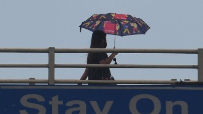 一名行人周一在烈日当空下，撑著伞走过菲律宾首都马尼拉的一座人行天桥。（图取自法新社）