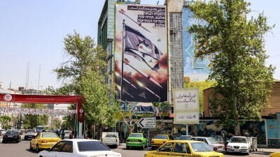 在伊朗德黑兰巴勒斯坦广场，车辆驶过一座建筑物，横幅上画著导弹和无人机飞过撕破的以色列国旗，上面用波斯语写著“下一巴掌会更重”，用希伯来语写著“你的下一个错误将是你虚假国家的终结”。（图取自法新社）