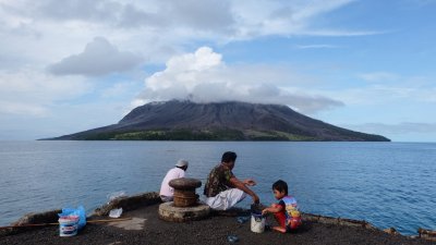 印尼北苏拉威西省塔古兰当岛的居民周五在一处港口钓鱼，对岸的鲁昂火山还冒著烟雾。（图取自法新社）