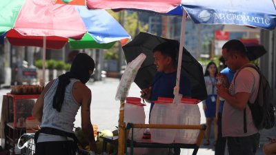 民众周三在菲律宾首都马尼拉的一条路上，购买椰子水来解渴降温。（图取自法新社）