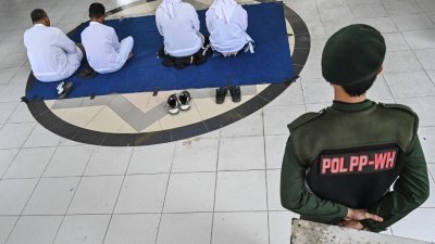周四在印尼班达亚齐，4名男女因违反伊斯兰教法而被判当众接受鞭刑之前，先接受宗教讲座开示，图中一名伊斯兰教警察在后面看守这4名男女。（图取自法新社）