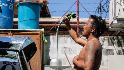 周日在菲律宾首都马尼拉，一名男子难忍炎热的天气在街上用软管淋浴消暑。（图取自法新社）