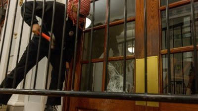 一名示威者周二凌晨在纽约市哥伦比亚大学校园内，打破一栋建筑的前门窗户，以便在上面系上链条，阻止当局进入。（图取自法新社）