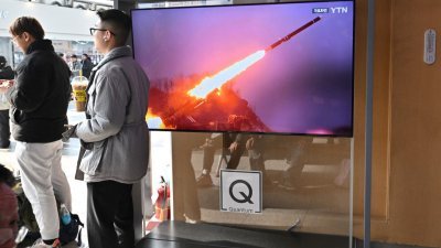 周五在韩国首尔的火车站，两名男子站在电视屏幕旁，电视正播放朝鲜试射导弹的新闻。（图取自法新社）