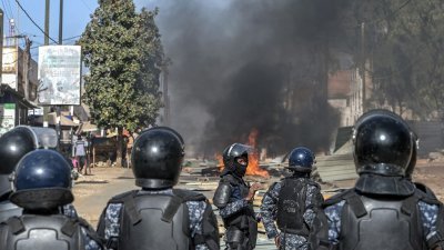 周日，塞内加尔首都达喀尔大批民众举行示威活动，警察在被纵火的路障前列队戒备。（图取自法新社）
