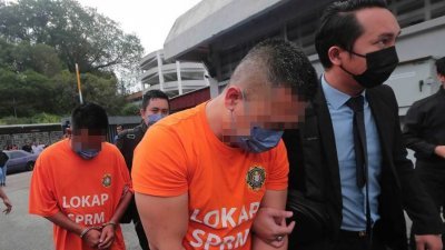 两名嫌犯（橙衣者）由反贪会官员押往新山推事庭申请延扣。