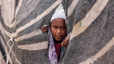 因以军攻击逃到拉法的加沙女孩，从难民营的一个帐篷探出头来，观察周围环境。（图取自法新社）