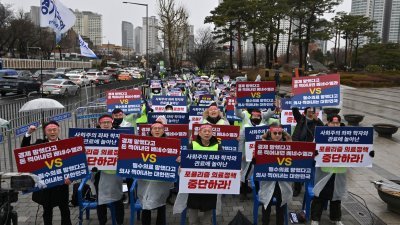 韩国医生举著写了“停止民粹主义医疗政策！”的标语牌，在首尔总统府附近参加集会，抗议政府提高医学院年度招生配额的计划。（图取自法新社）