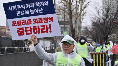 一名韩国医生上周三与其他医生在首尔总统府附近举行集会，抗议政府提高医学院年度招生配额的计划，他高举著标语牌，上面写著“停止民粹主义医疗政策”。（图取自法新社）