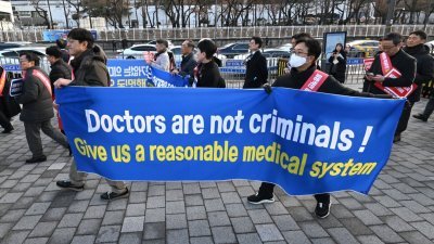 韩国医生们在周日的集会走向总统府期间，举著“医生不是罪犯！”的布条。（图取自法新社）