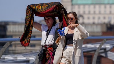 2022年7月18日，英国遭遇热浪期间，在伦敦千禧桥上的一名妇女高举披肩遮挡阳光。（图取自路透社档案照）