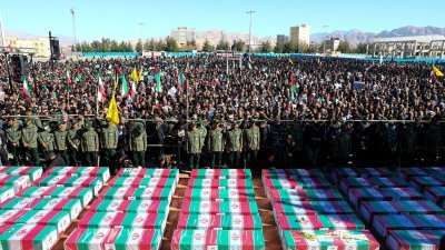 伊朗官员与民众周五参加克尔曼爆炸袭击事件死难者的葬礼，棺木覆盖国旗，众人为死者祈祷。（图取自路透社）