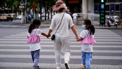 中国上海市一名母亲牵著她的双胞胎女儿，走过斑马线。（图取自路透社）