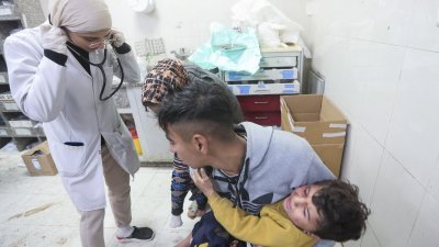 一名巴勒斯坦人周一抱著一名在以色列袭击纳赛尔医院时受伤的儿童。（图取自路透社）