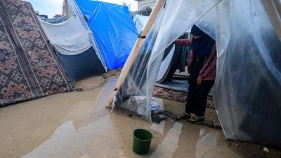 在加沙难民营，一名巴勒斯坦妇女无奈地站在被大雨淹没的帐篷入口。（图取自法新社）