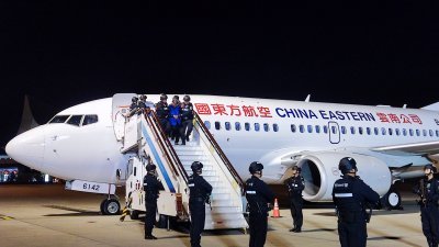 中国云南公安机关民警周二包机，将10名缅北电诈犯罪集团头目和4名重大嫌犯押解回国。包机降落在昆明长水机场，警员将他们一个一个地带出飞机。（图取自中新社/中国公安部供图）