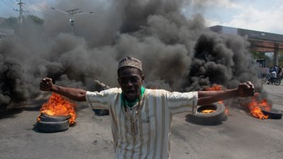 海地黑帮暴力骚乱持续延烧，图为周二在总理亨利宣布辞职后，一名抗议者在街上示威，有轮胎在其身后燃烧。（图取自法新社）