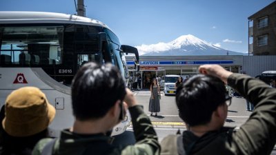 周五在当局架设一个巨大布幕以阻拍富士山前，游客试图在话题便利商店外拍摄照片。（图取自法新社）