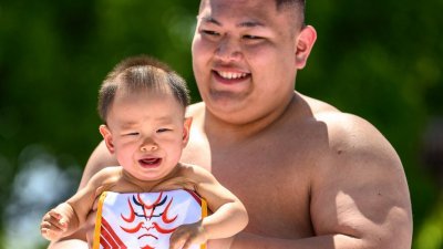 日本一名相扑选手抱著一名婴儿，参加日前在东京浅草寺举行的哭泣宝宝相扑活动。（图取自法新社）