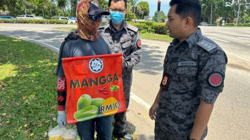 移民局执法人员调查在路上非法售卖罐装腌芒果的外劳。（照片取自网络）