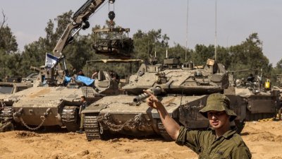 一名以色列士兵上周二在以色列南部靠近加沙的边界，在起重机吊起主战坦克发动机时打手势。（图取自法新社）