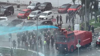 演习中，水炮车喷出蓝色水柱驱散滋事者，防暴警察手持盾牌组成防线，场面逼真。（图：霹雳警方）