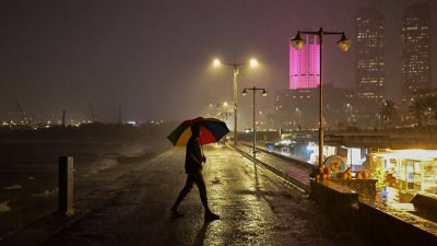 一名男子周一在雨中撑伞，走过斯里兰卡科伦坡加勒菲斯海滨步道。（图取自法新社）

