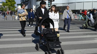 一对男女周三在中国首都北京市推著婴儿车穿过街道。（图取自法新社）