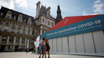 法国正面临新一波疫情，政府呼吁老年人和脆弱人群须及时接种第4剂疫苗。两名女子去年7月，走过设置在法国巴黎市政厅前的新冠肺炎疫苗接种中心。（图取自路透社档案照）